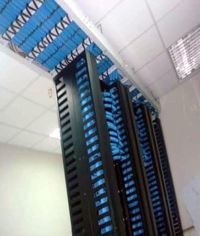 Open-bay racks with blue patch cords beneath a ceiling-mounted cable tray